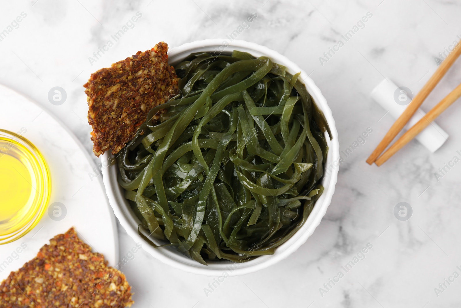 Photo of Tasty seaweed salad in bowl served on white marble table, flat lay