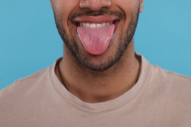 Photo of Happy man showing his tongue on light blue background, closeup