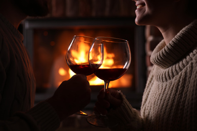 Lovely couple with glasses of wine near fireplace at home, closeup. Winter vacation