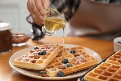 Woman pouring honey onto delicious Belgian waffles  at wooden table in kitchen, closeup