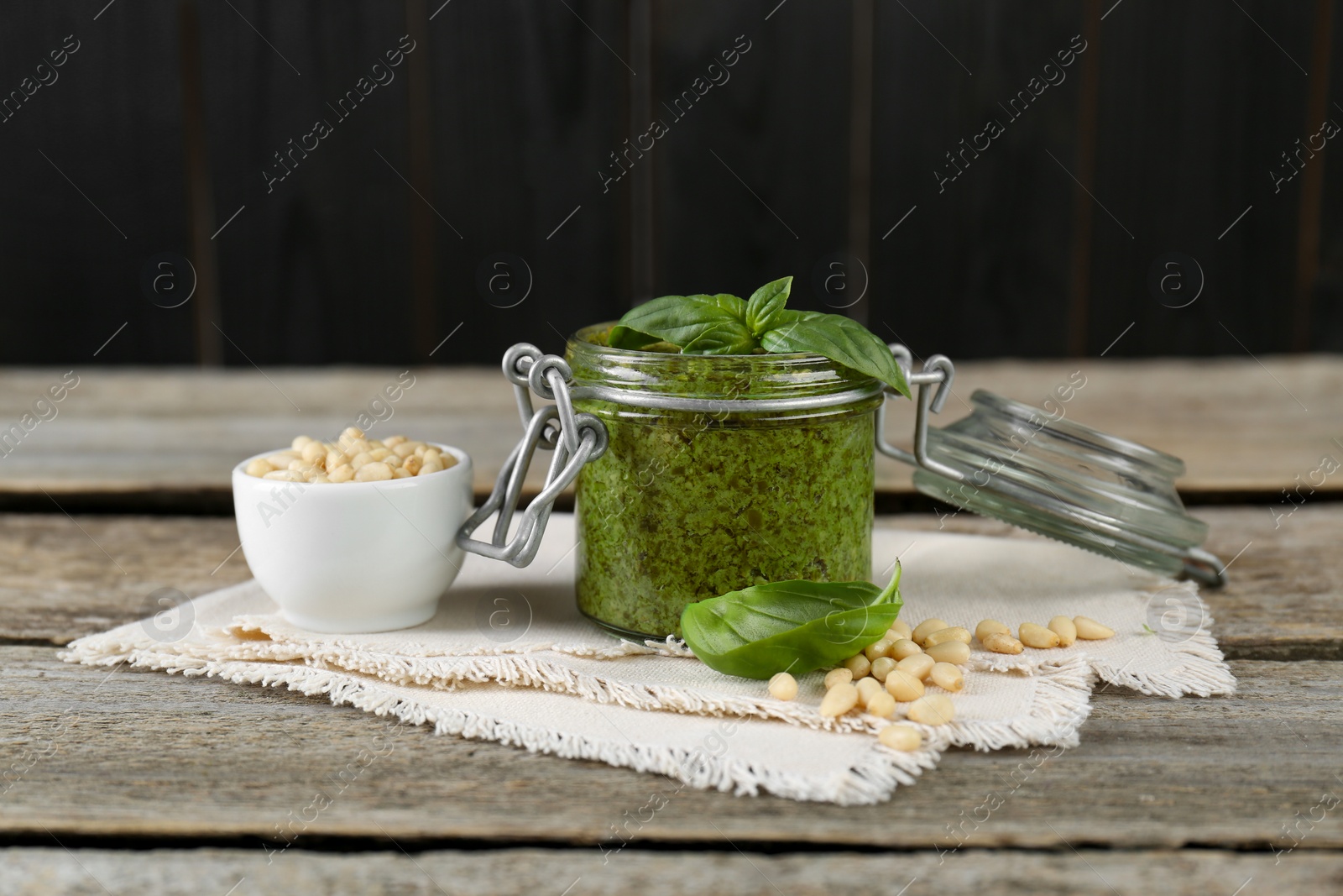 Photo of Delicious pesto sauce, pine nuts and basil leaves on wooden table