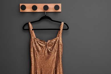Photo of Beautiful golden women's party dress on hanger near grey wall, space for text. Stylish trendy clothes for high school prom