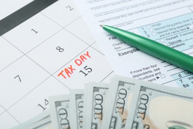 Photo of Tax day. Document, dollar banknotes and pen on calendar with date reminder