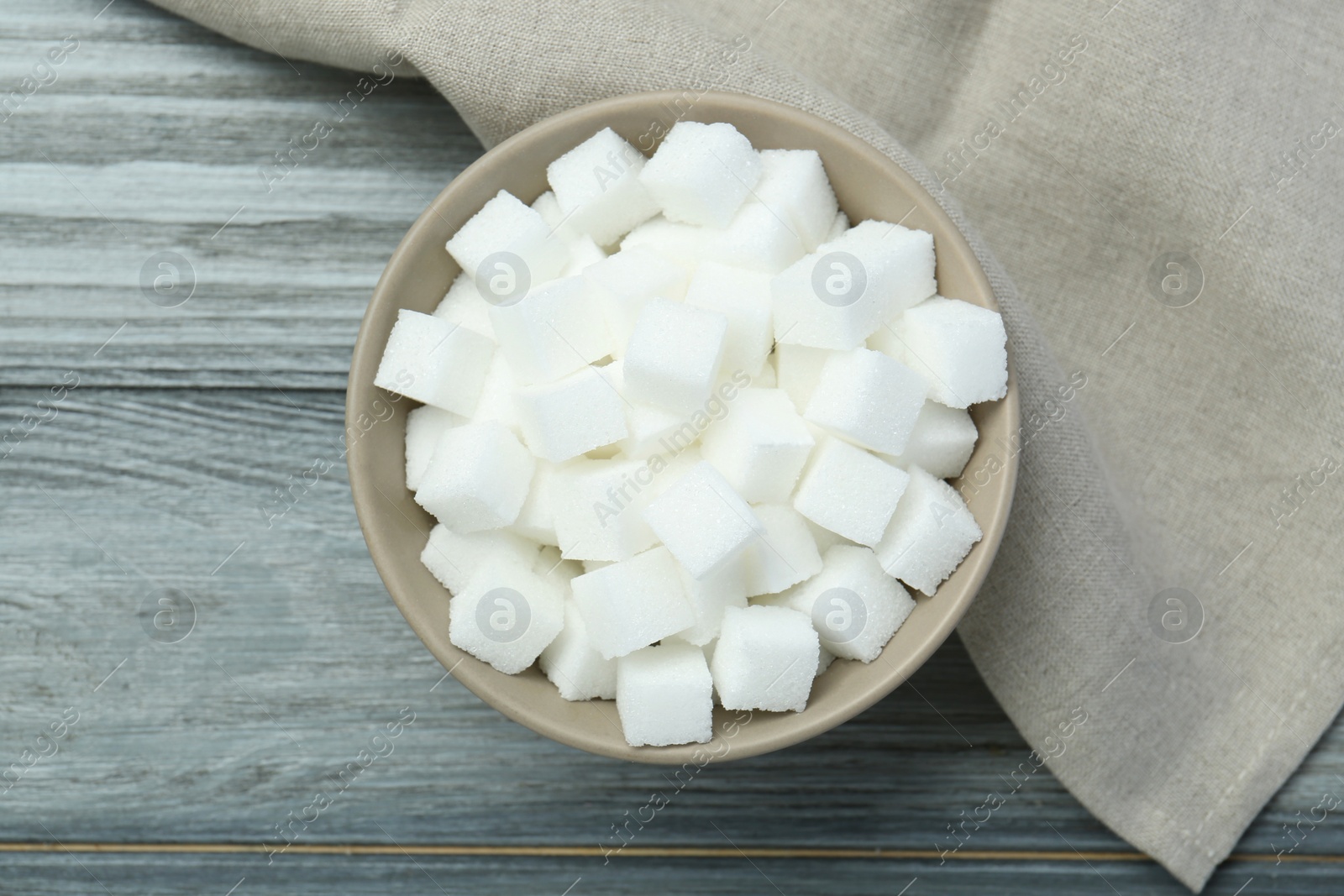 Photo of White sugar cubes in bowl on wooden table, top view