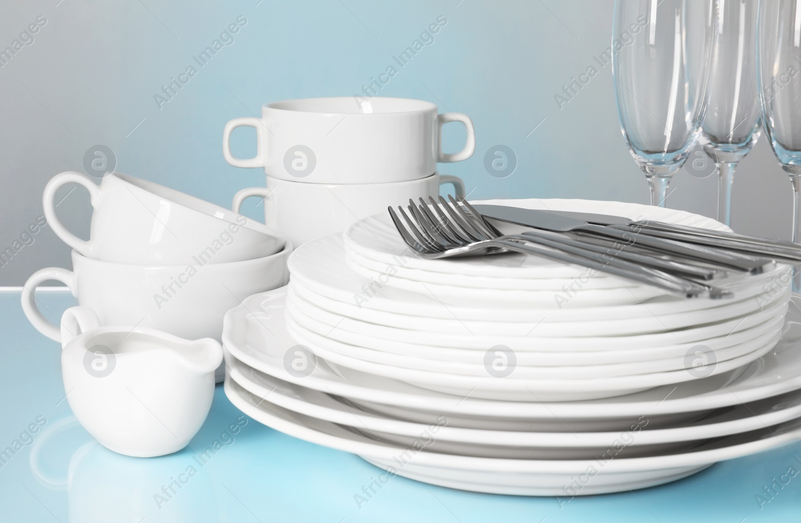 Photo of Set of clean dishes, glasses and cutlery on light blue table, closeup