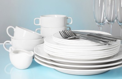 Set of clean dishes, glasses and cutlery on light blue table, closeup