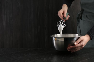 Photo of Woman making whipped cream with whisk at black table, closeup. Space for text