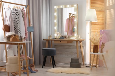 Photo of Makeup room. Stylish dressing table with mirror, chair and clothes rack indoors