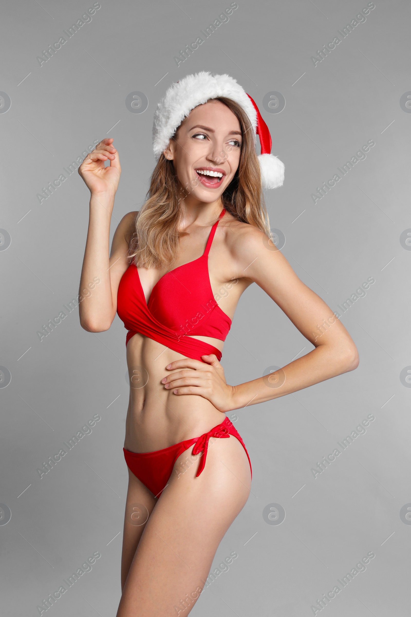 Photo of Happy young woman in red bikini and Santa hat on light grey background. Christmas celebration