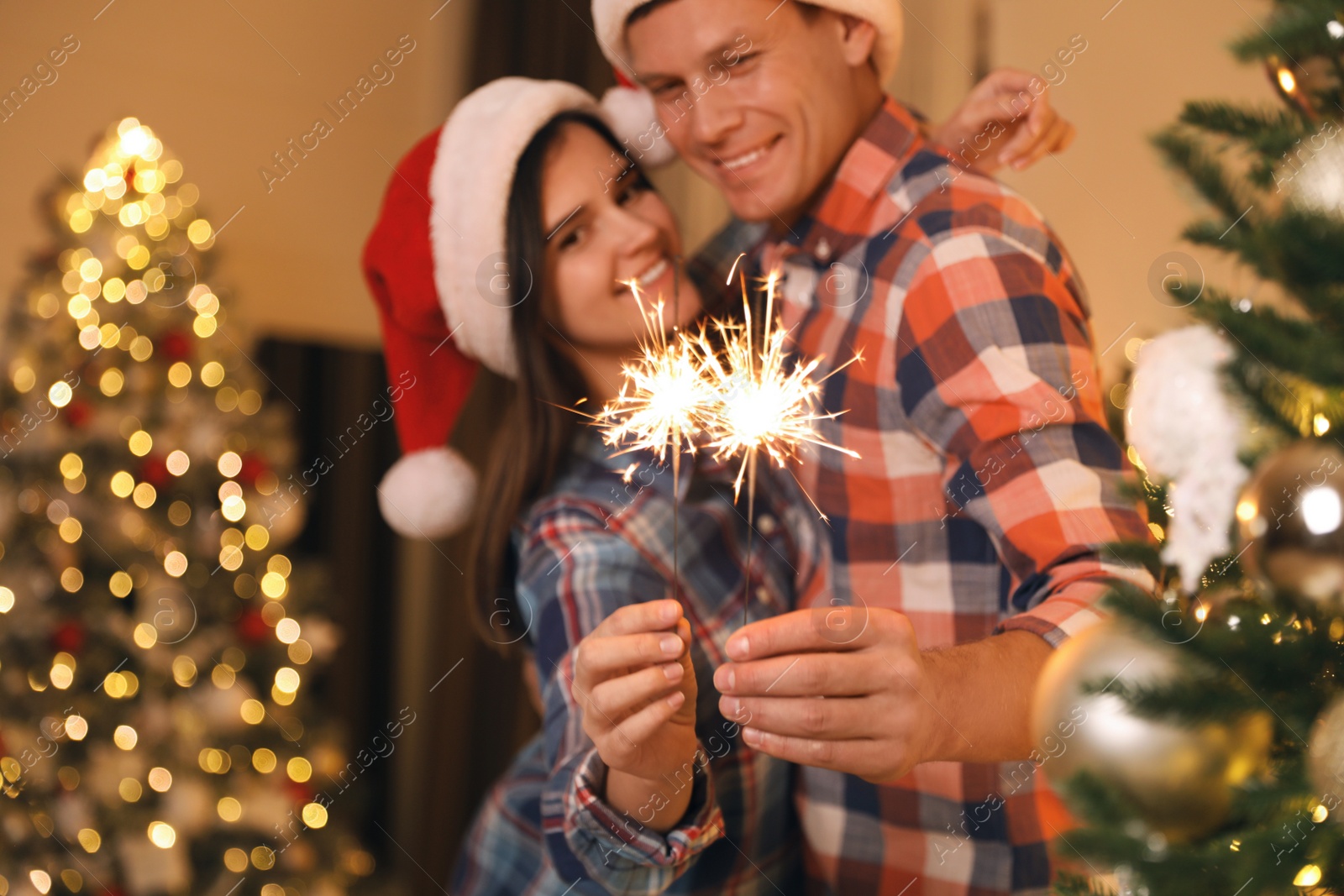 Photo of Couple holding sparkles in room decorated for Christmas, focus on fireworks