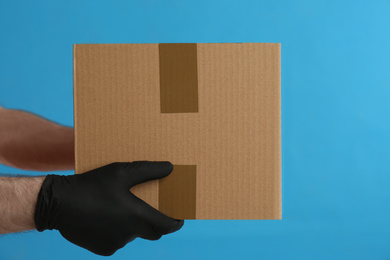 Photo of Courier holding cardboard box on blue background, closeup. Parcel delivery