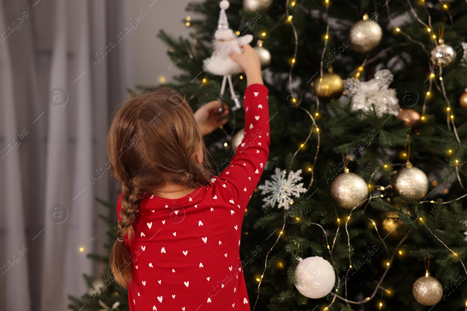 Photo of Cute little child decorating Christmas tree at home, back view