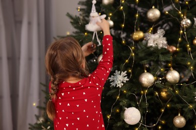 Cute little child decorating Christmas tree at home, back view