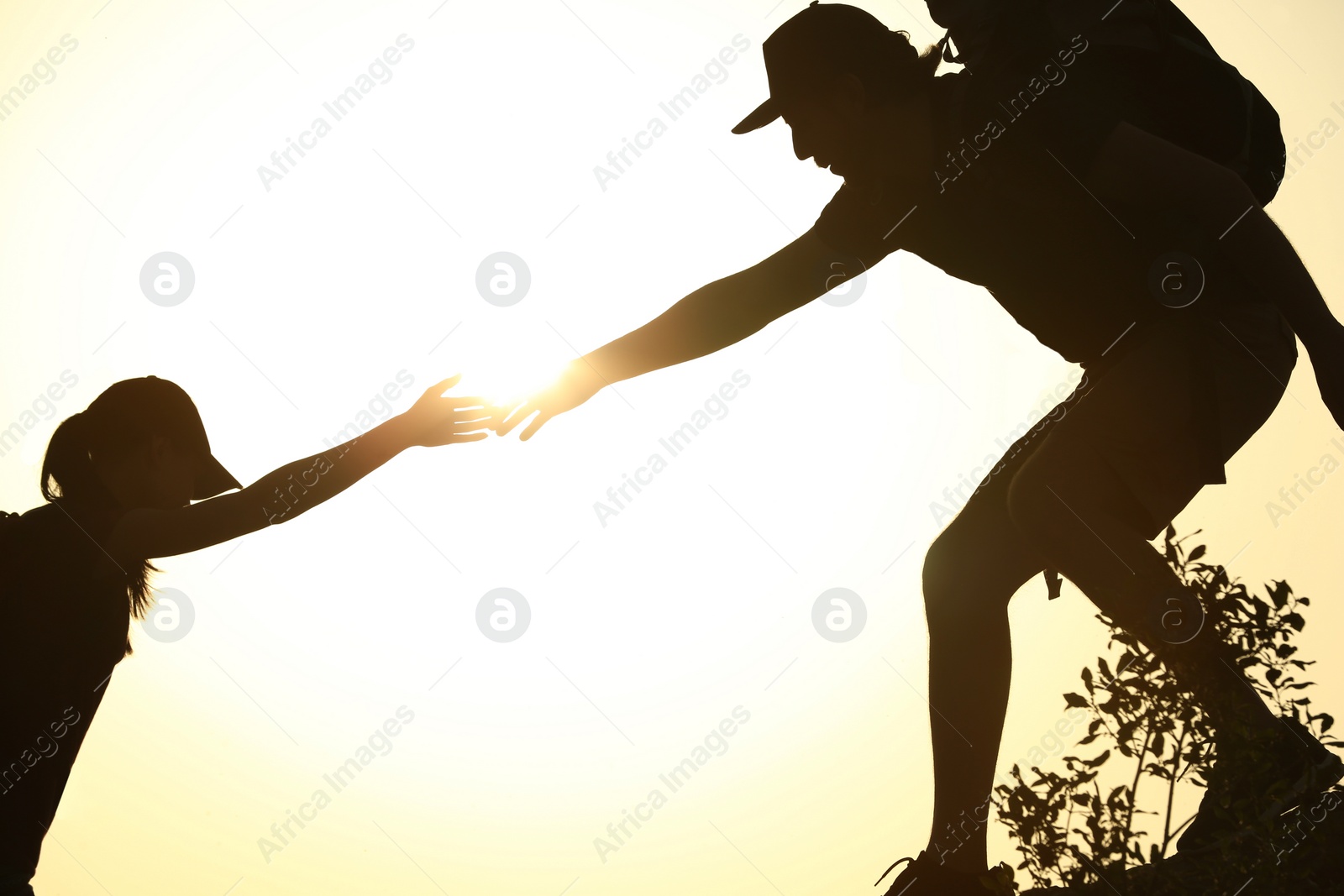 Photo of Silhouettes of man and woman helping each other to climb on hill against sunset