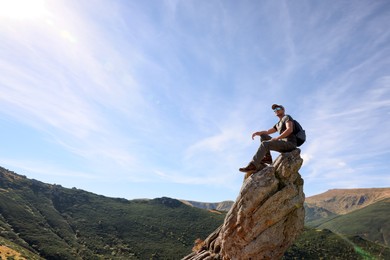 Photo of Man with backpack on rocky peak in mountains. Space for text
