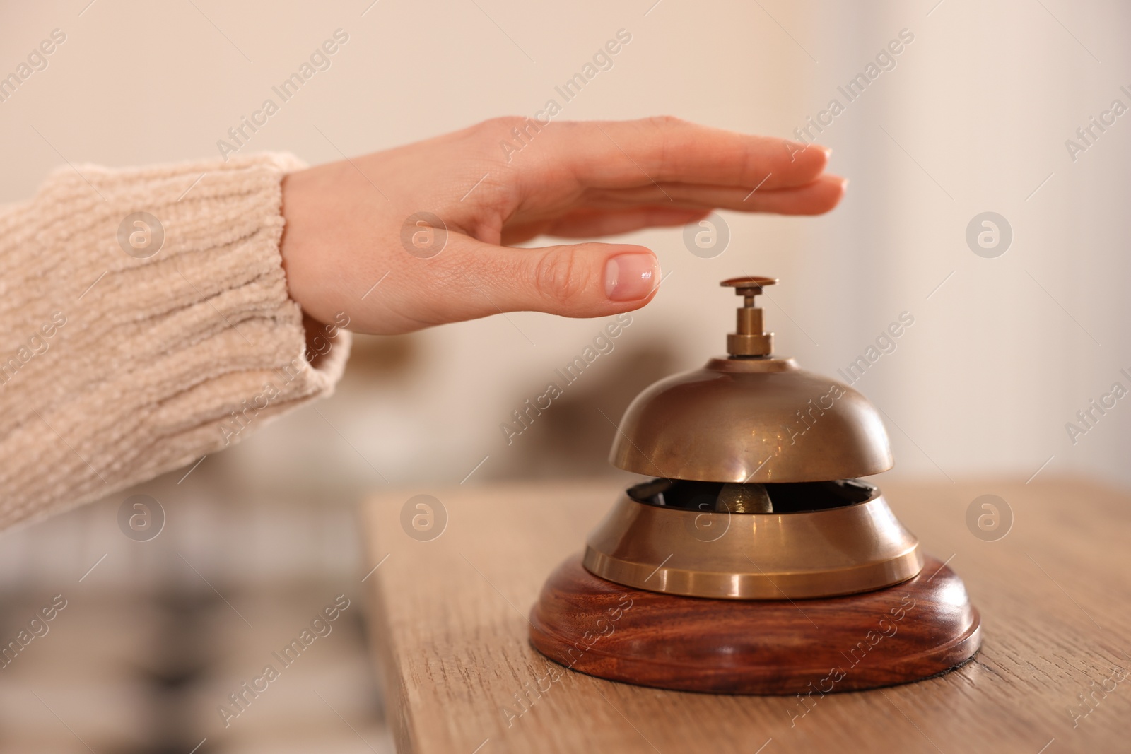 Photo of Woman ringing hotel service bell at wooden reception desk, closeup