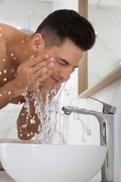 Photo of Handsome man washing face over sink in bathroom