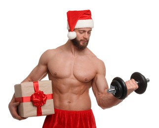 Attractive young man with muscular body in Santa hat holding Christmas gift box and dumbbell on white background