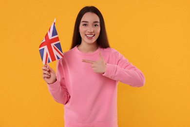 Young woman holding flag of United Kingdom on orange background