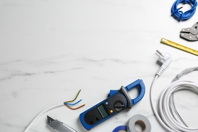Photo of New wires and electrician's tools on white marble table, flat lay. Space for text