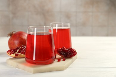 Photo of Tasty pomegranate juice in glasses and fresh fruits on white wooden table, closeup. Space for text