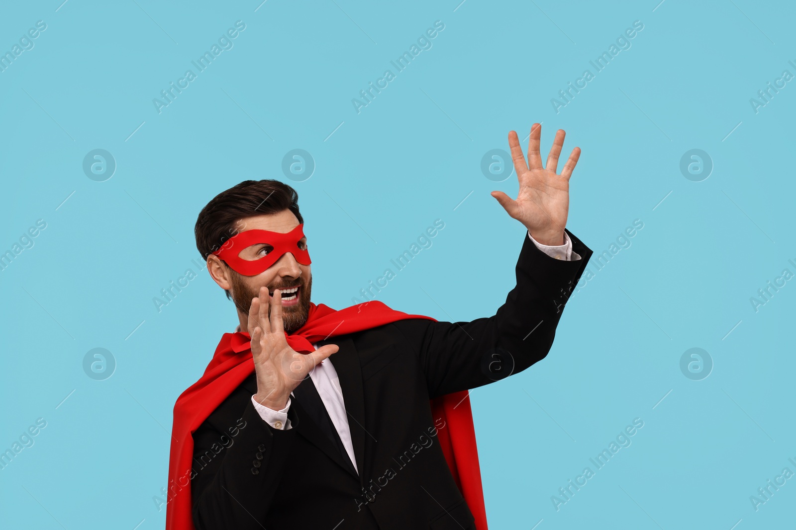 Photo of Businessman wearing red superhero cape and mask on light blue background