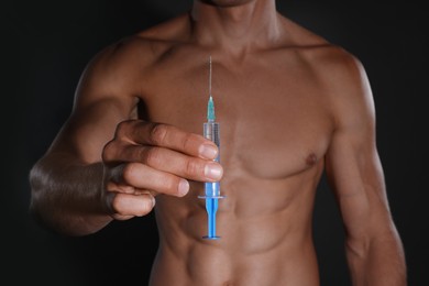 Athletic man with syringe against black background, closeup. Doping concept