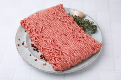 Photo of Fresh raw ground meat, peppercorns, garlic and thyme on white tiled table, closeup