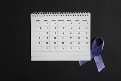 Purple awareness ribbon and calendar on black background, top view
