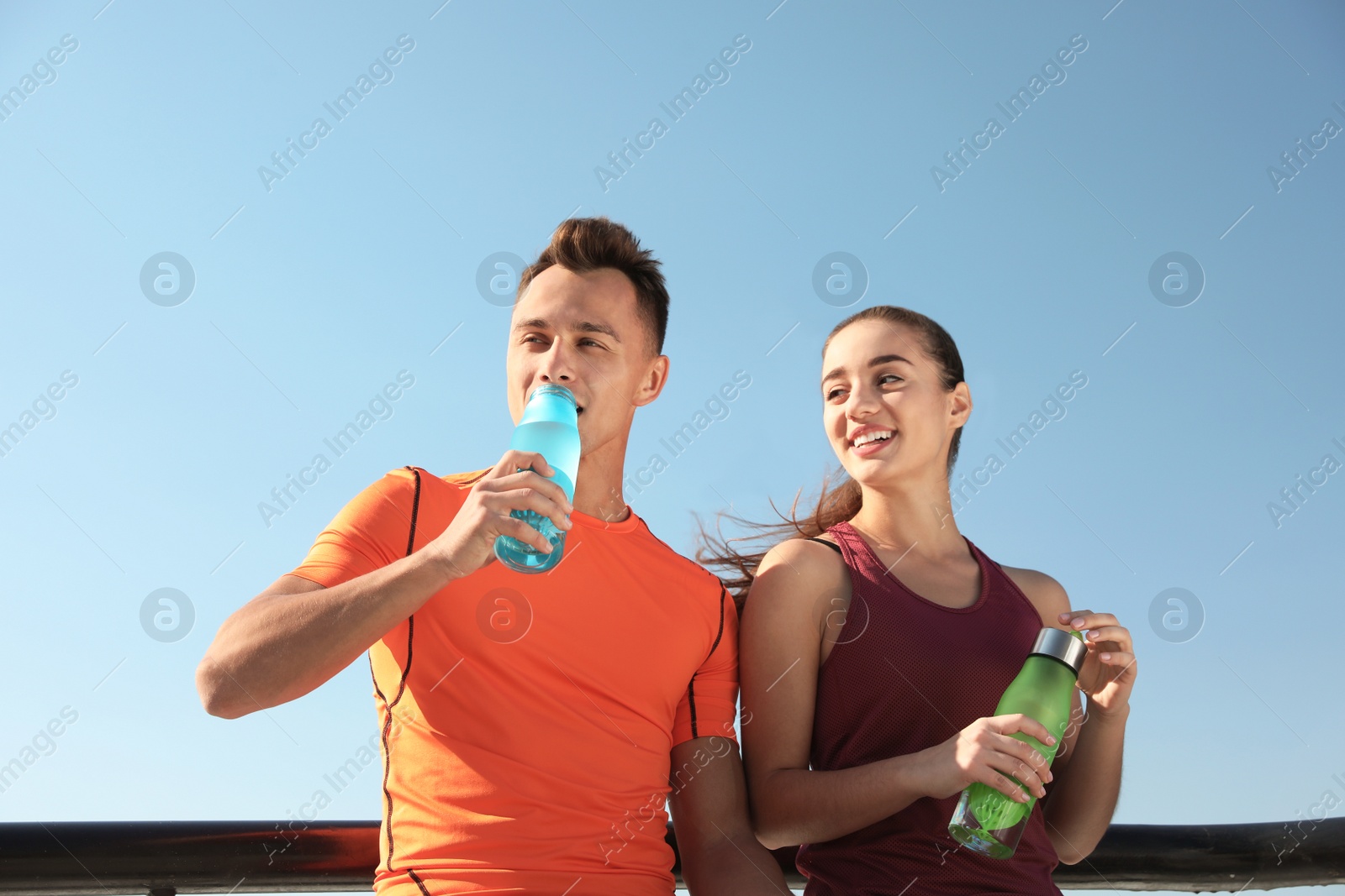 Photo of Young sporty couple with bottles of water outdoors on sunny day