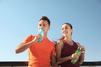 Photo of Young sporty couple with bottles of water outdoors on sunny day