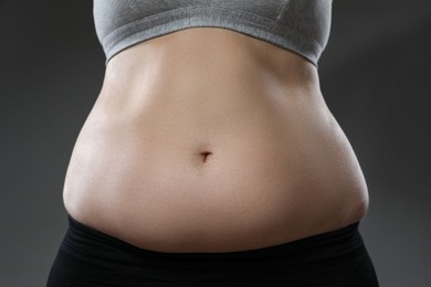 Woman with excessive belly fat on grey background, closeup. Overweight problem