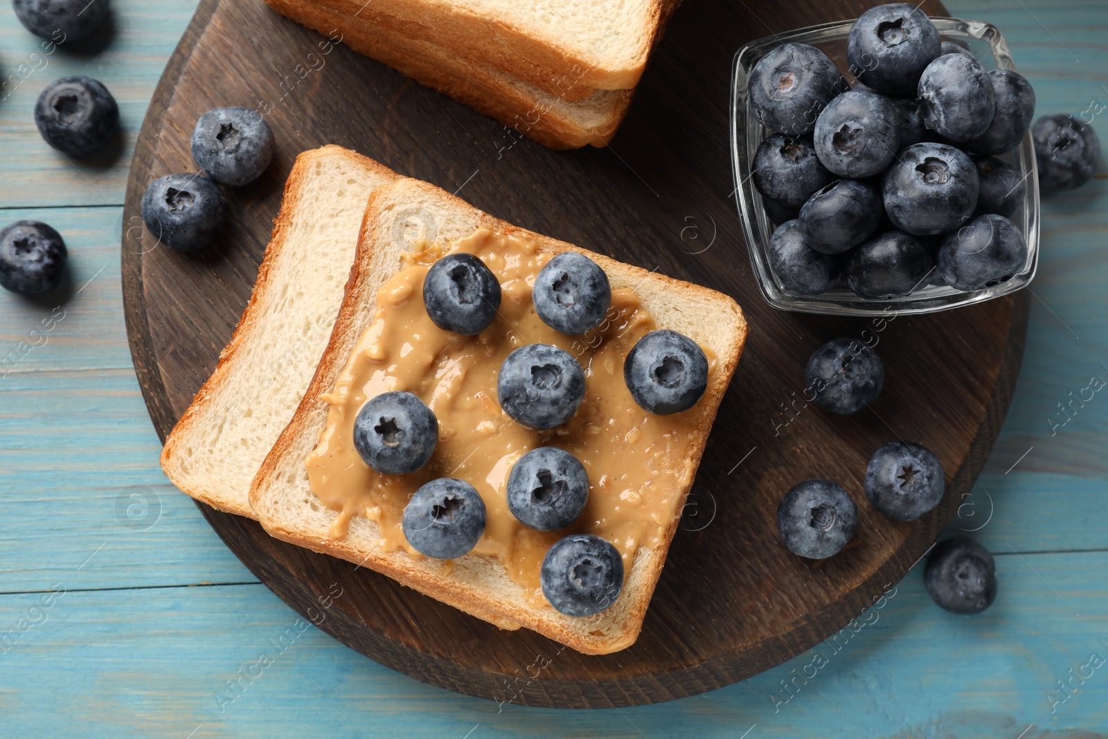 Photo of Delicious toasts with peanut butter and blueberries on light blue wooden table, top view