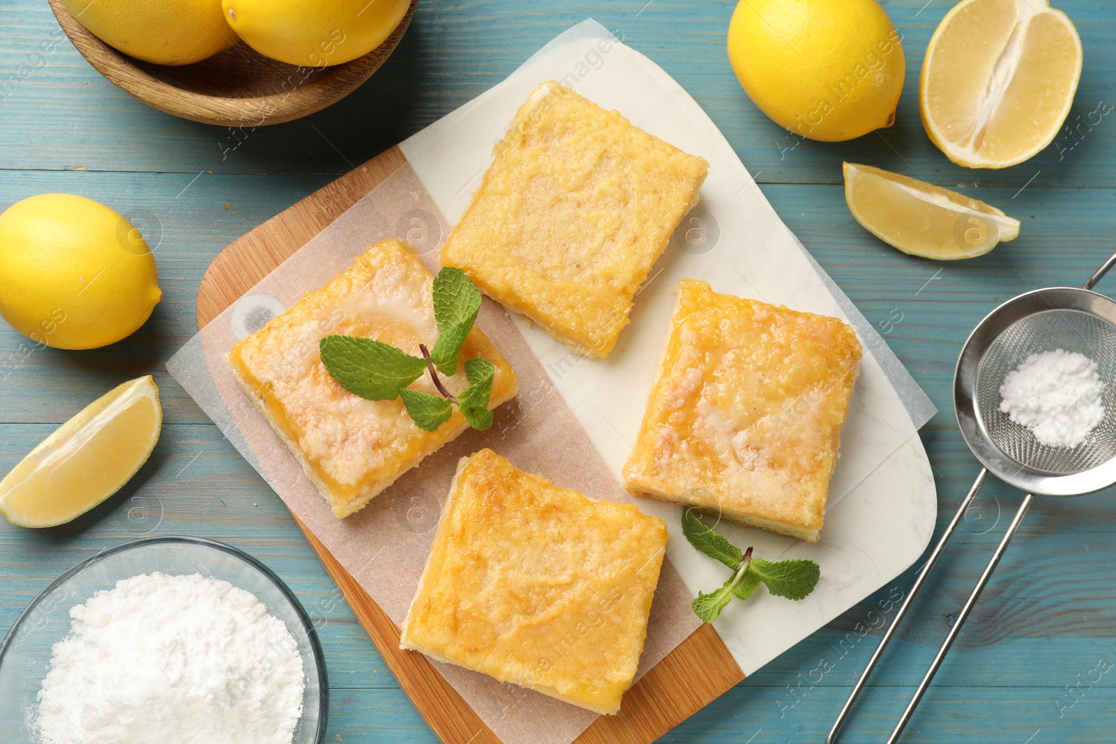 Photo of Tasty lemon bars and mint on light blue wooden table, flat lay