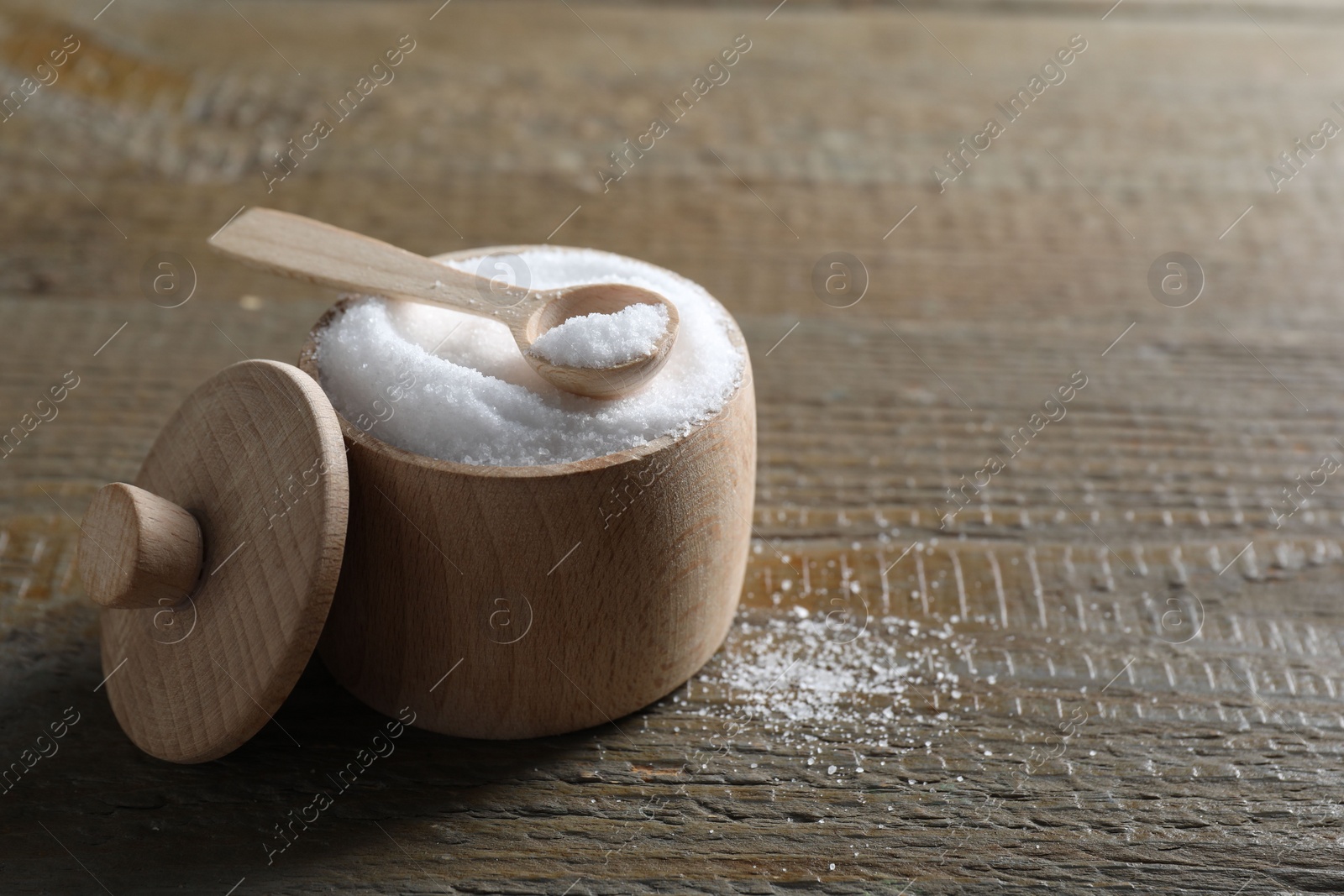 Photo of Organic salt in bowl and spoon on wooden table, closeup. Space for text