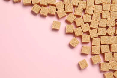 Photo of Brown sugar cubes on pink background, flat lay. Space for text