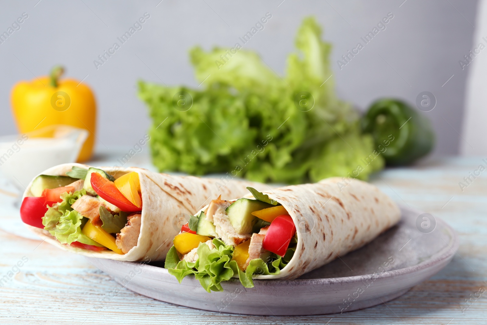 Photo of Plate with delicious meat tortilla wraps on white wooden table against grey background