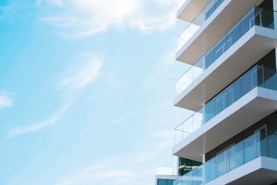 Photo of Exterior of residential building with balconies against blue sky, low angle view. Space for text