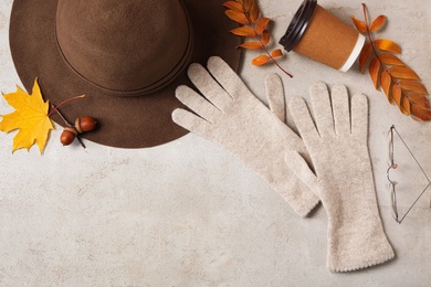 Photo of Flat lay composition with stylish woolen gloves, hat and dry leaves on beige table. Space for text