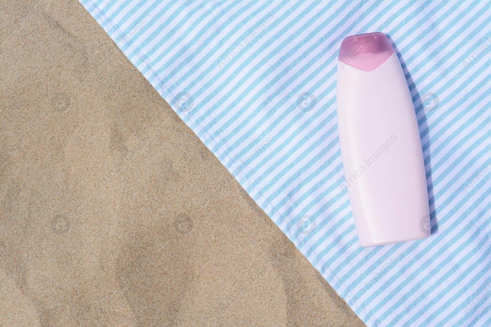 Photo of White and light blue striped towel with bottle of sunblock on sandy beach, top view. Space for text