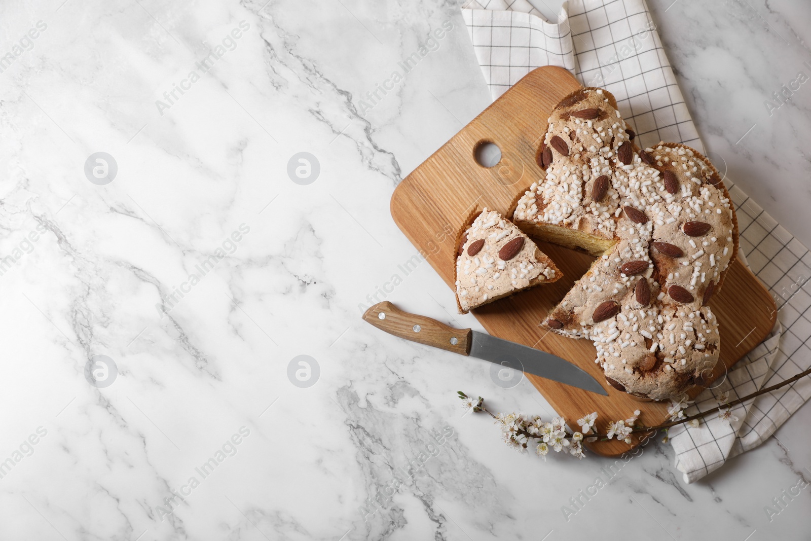Photo of Delicious Italian Easter dove cake (traditional Colomba di Pasqua), knife and branch with beautiful flowers on white marble table, top view. Space for text