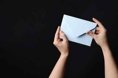 Woman holding white paper envelope on black background, closeup. Space for text