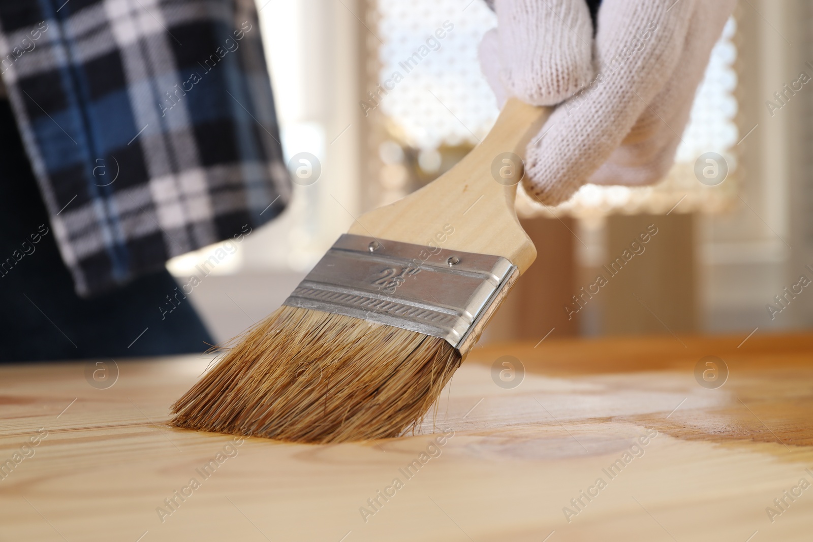 Photo of Man with brush applying wood stain onto wooden surface indoors, closeup