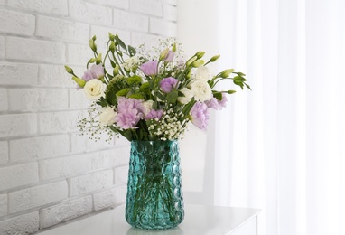 Photo of Bouquet of beautiful Eustoma flowers on table near white brick wall