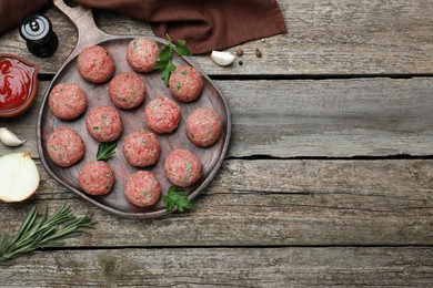 Photo of Many fresh raw meatballs and ingredients on wooden table, flat lay. Space for text