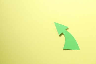 Photo of Curved green paper arrow on yellow background, top view. Space for text