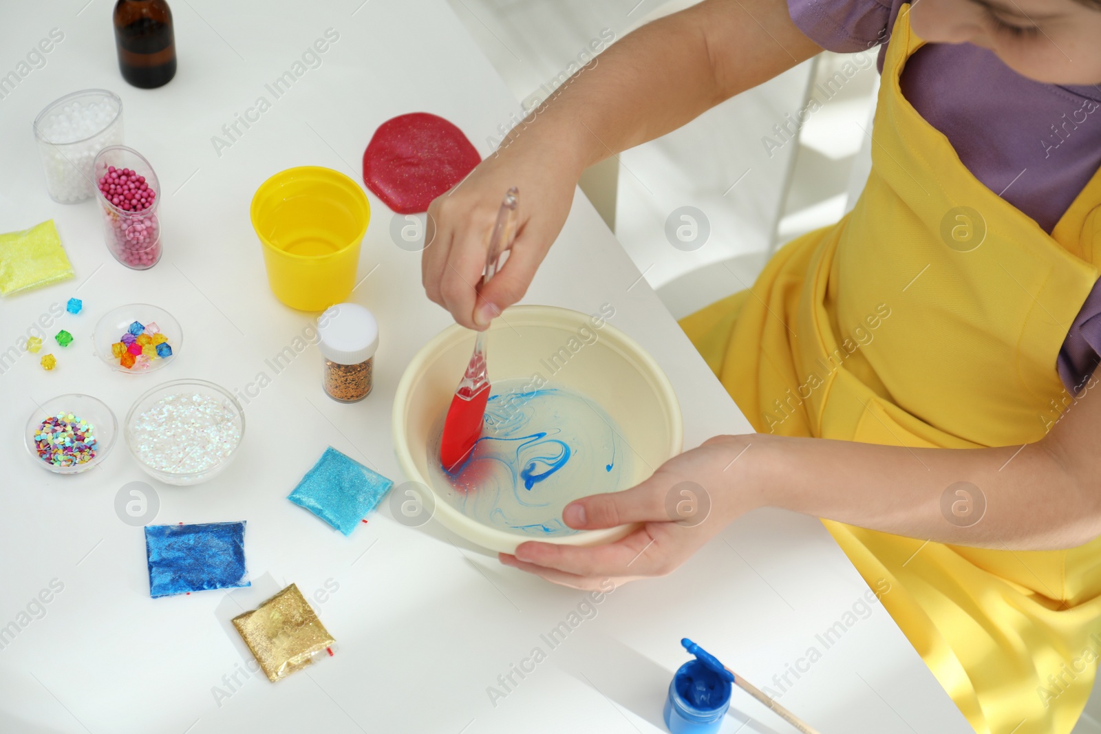 Photo of Little girl mixing ingredients with silicone spatula at table, closeup. DIY slime toy