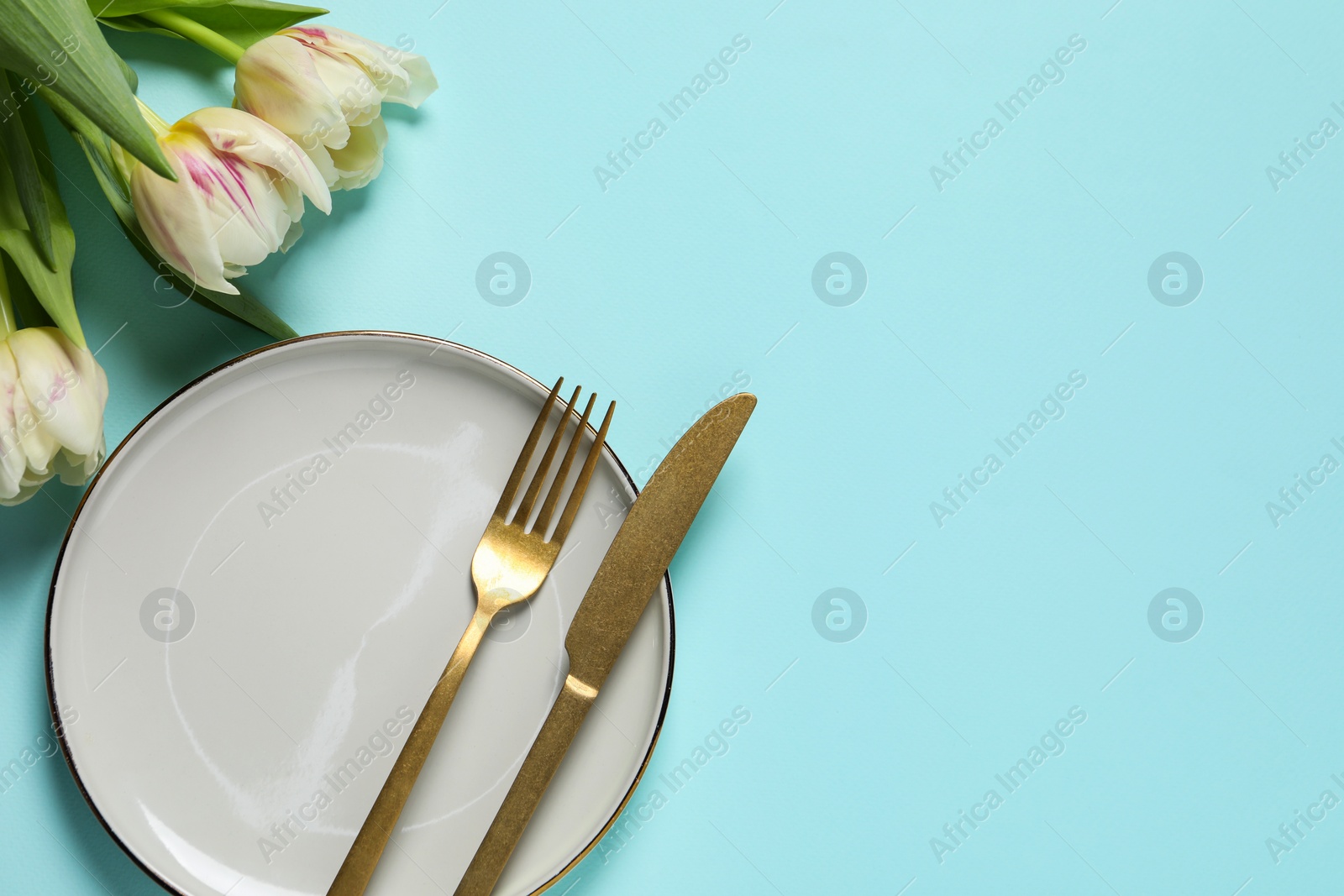 Photo of Stylish table setting with cutlery and tulips on light blue background, flat lay. Space for text