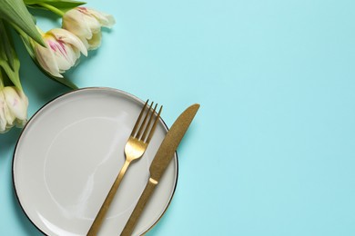 Stylish table setting with cutlery and tulips on light blue background, flat lay. Space for text