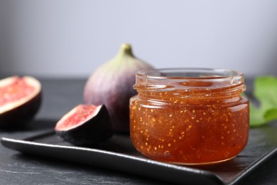 Photo of Jar of tasty fig jam and fresh fruits on black table, closeup. Space for text